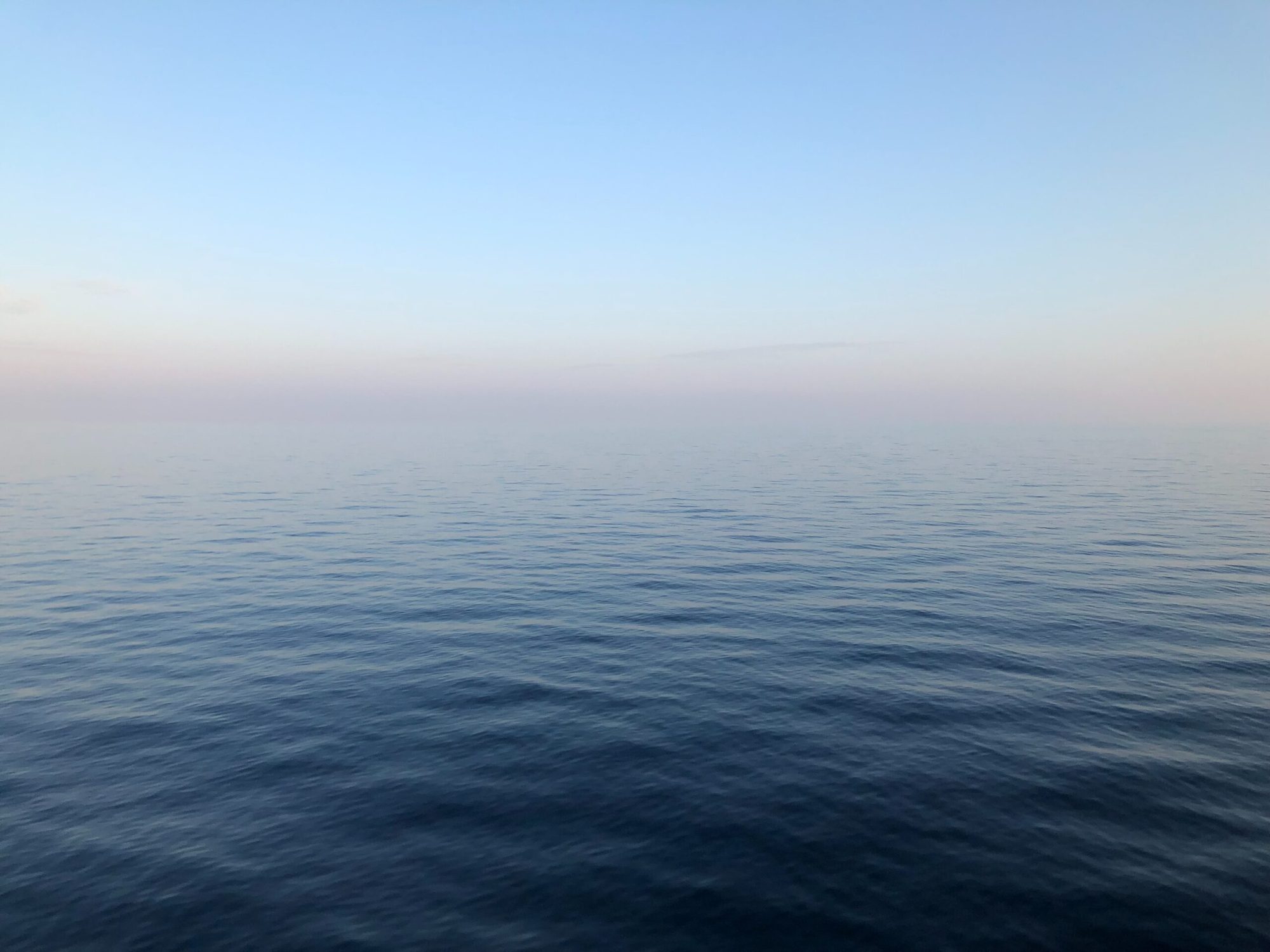 Calm open sea at dawn, meeting a pale blue sky